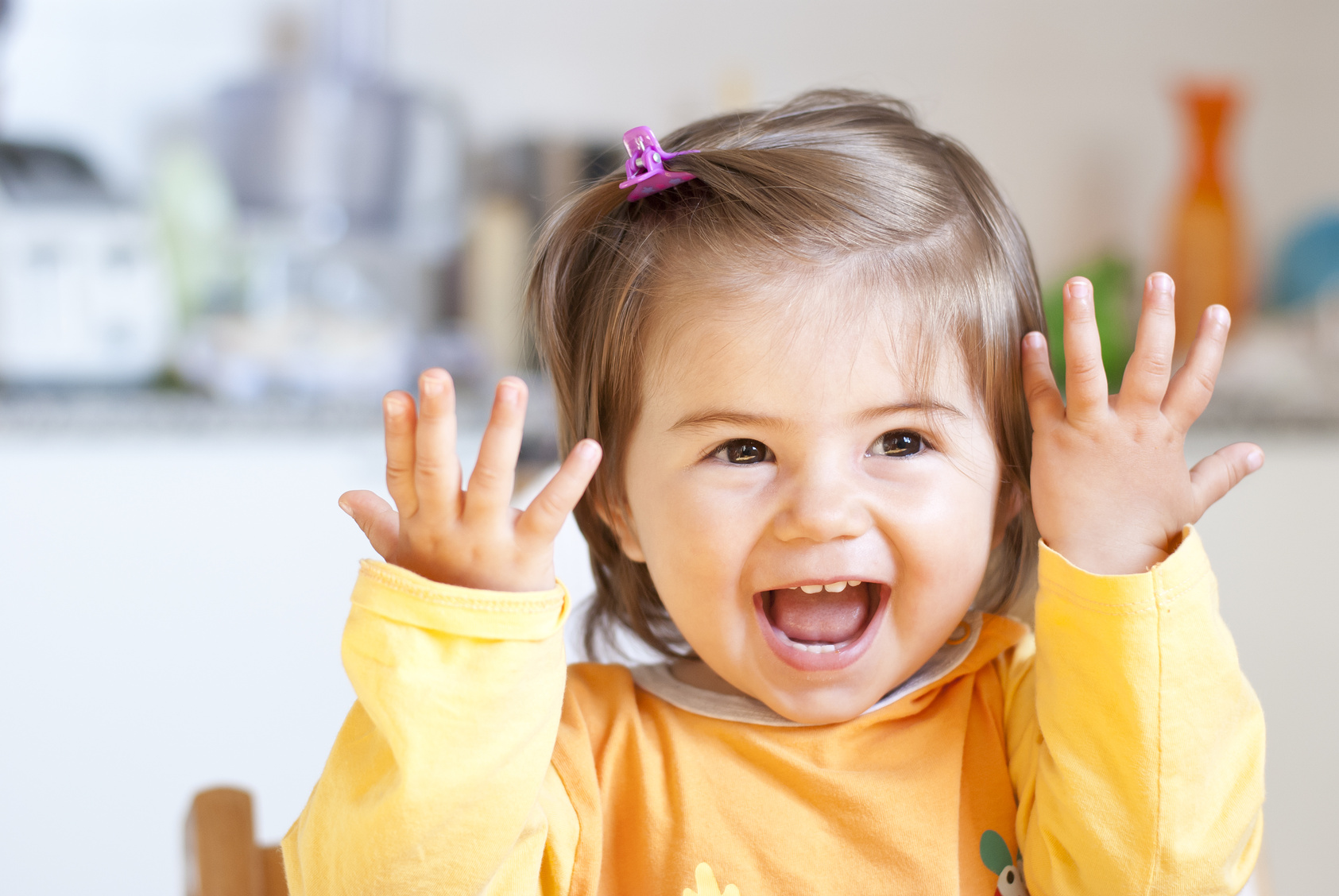 Smiling toddler in yellow jumper holding her hands up