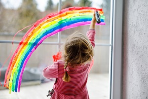 Young girl painting a rainbow on a window