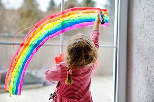 Young girl painting a rainbow on a window