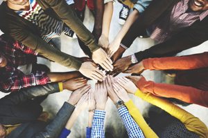 People in a circle holding hands in the centre, many different skin colours