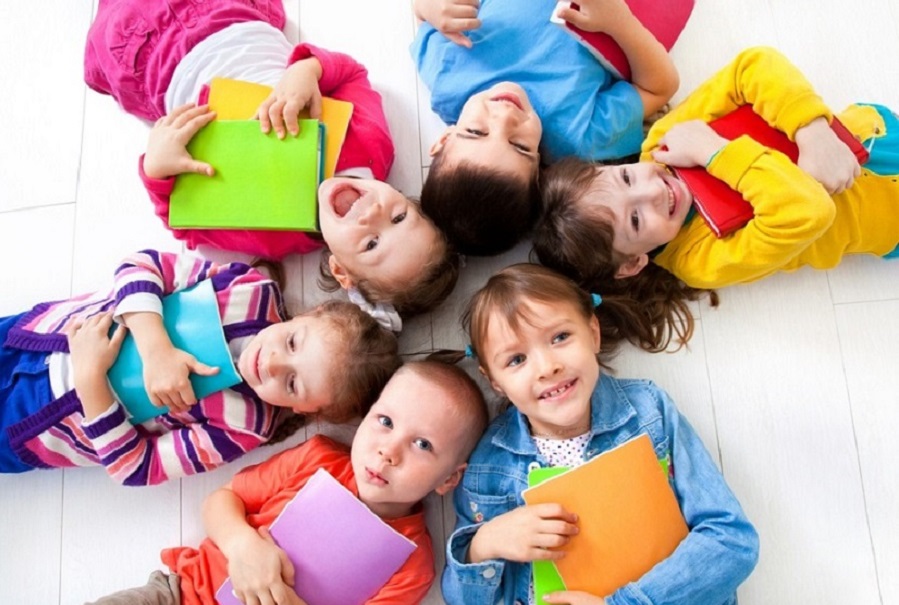 Smiling children laying in a circle holding schoolbooks