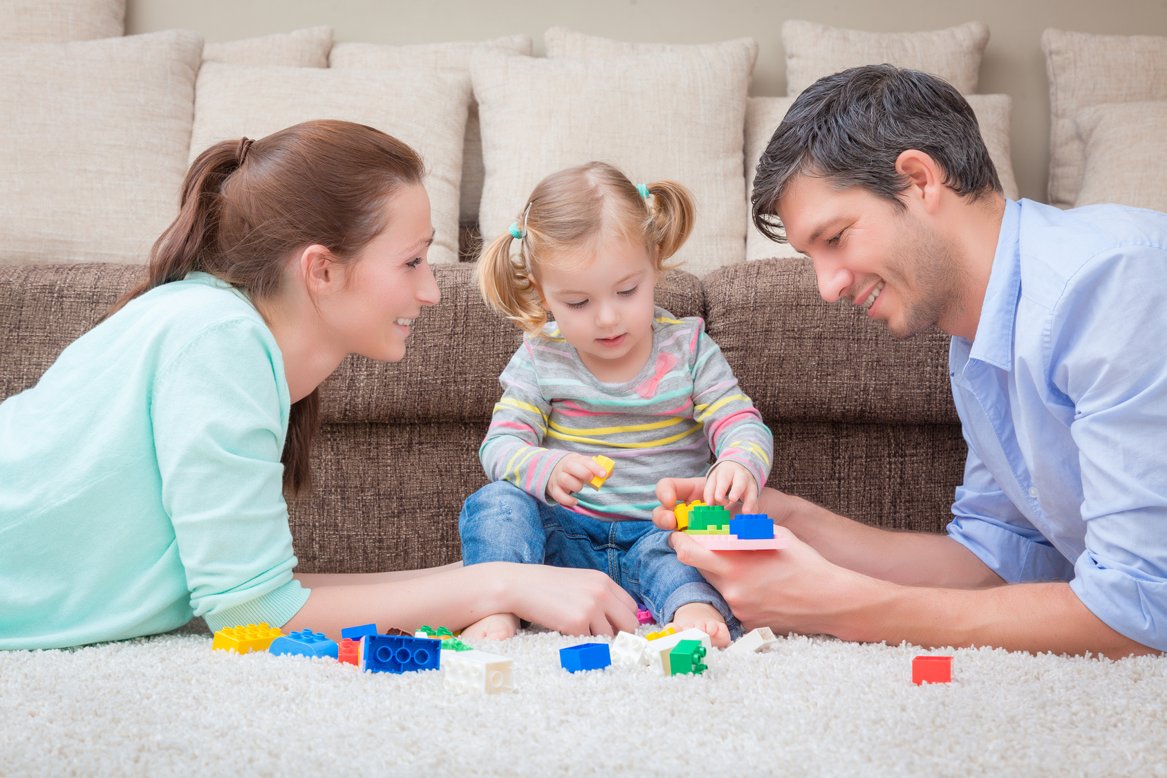 Man and woman lying on stomachs playing with a toddler girl