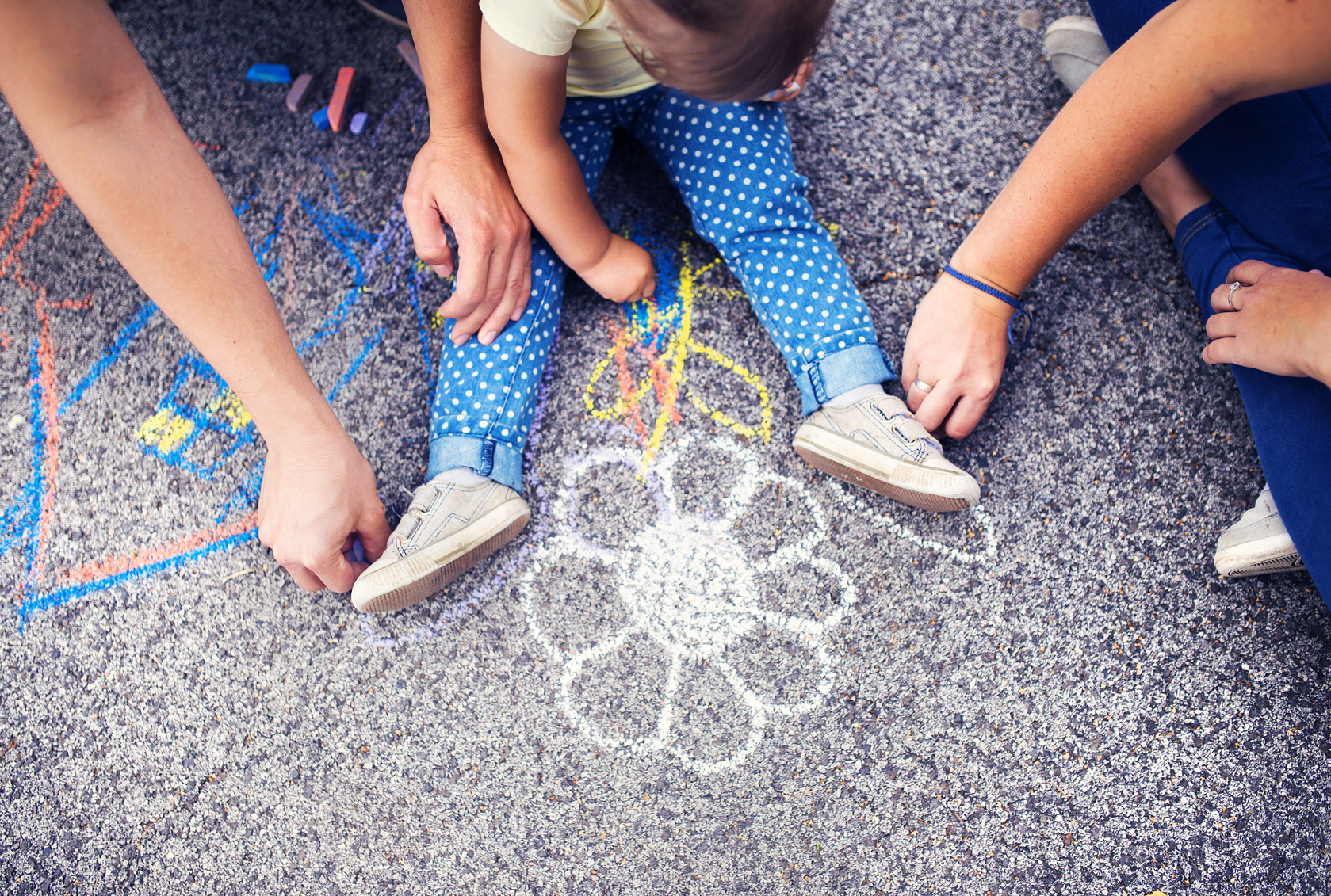 Image of children's legs on the ground and hands using chalk to draw a flower