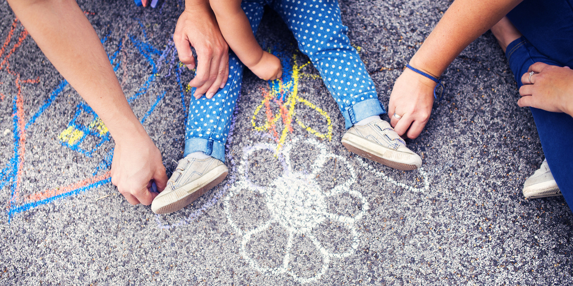 Image of children's legs on the ground and hands using chalk to draw a flower