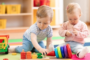 Toddler boy and girl playing with coloured blocks on a mat