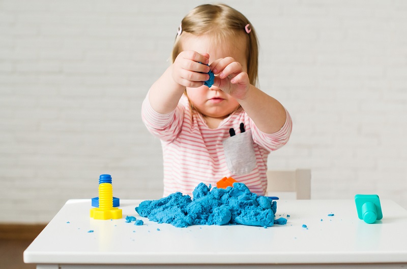 Toddler girl playing with blue kinetic sand