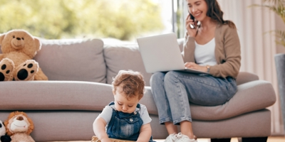 Woman on a phone call with a laptop on her lap watching a toddler play with an abacus