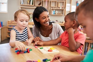 Nursery practitioner seated at table with young children