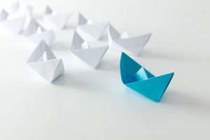 blue paper boat leading other boats