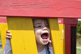Child shouting through wooden slats on colourful play equipment