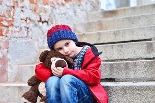 Sad boy sitting holding his teddy bear on steps outdoors