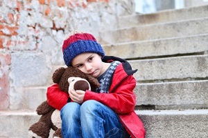 Sad boy sitting holding his teddy bear on steps outdoors